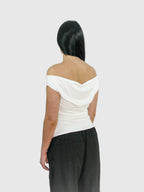 Person wearing a white off-shoulder top and black pants on a plain background