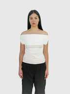 Woman wearing a white off-shoulder top and black pants against a plain background