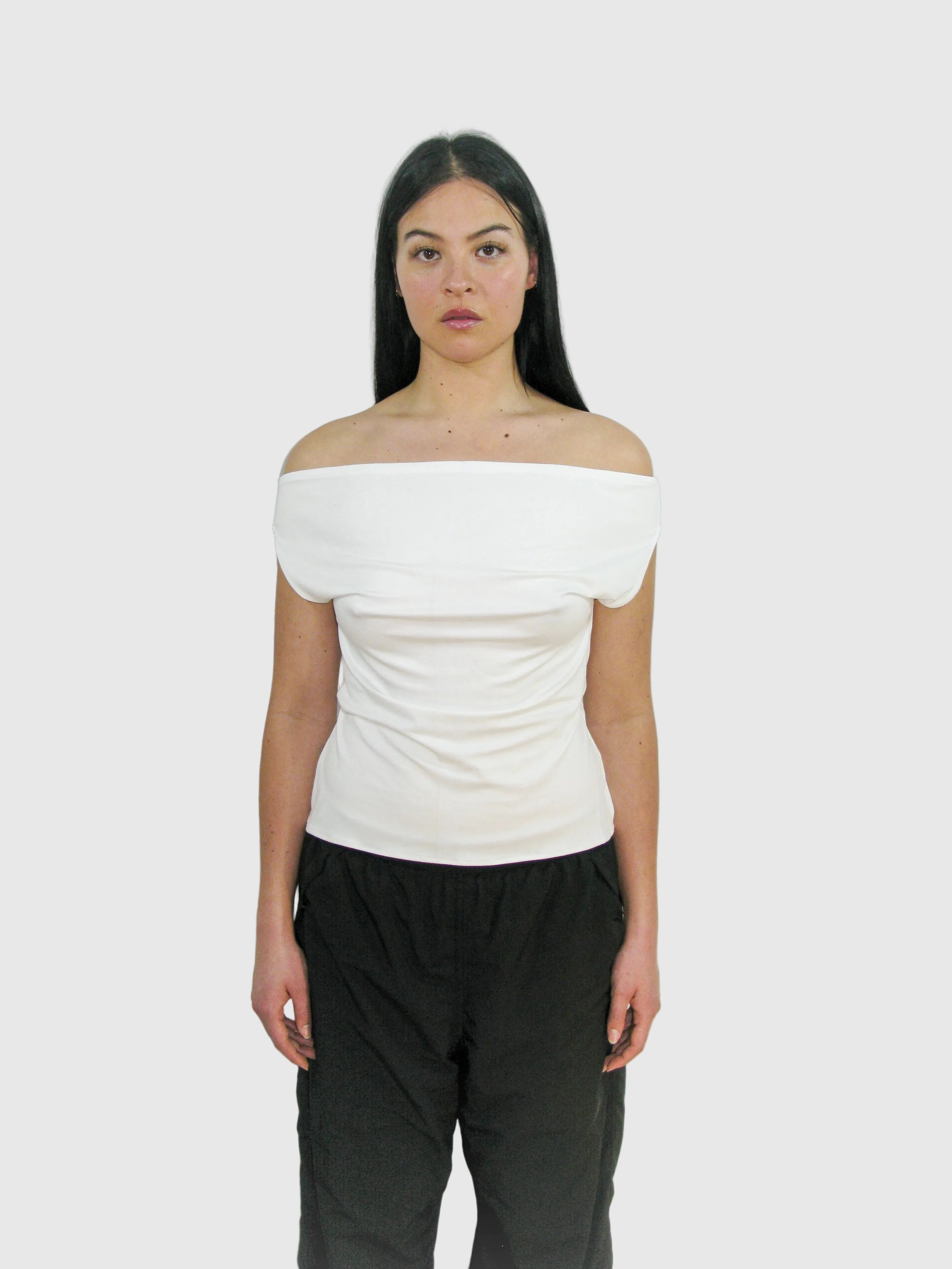 Woman wearing a white off-shoulder top and black pants against a plain background