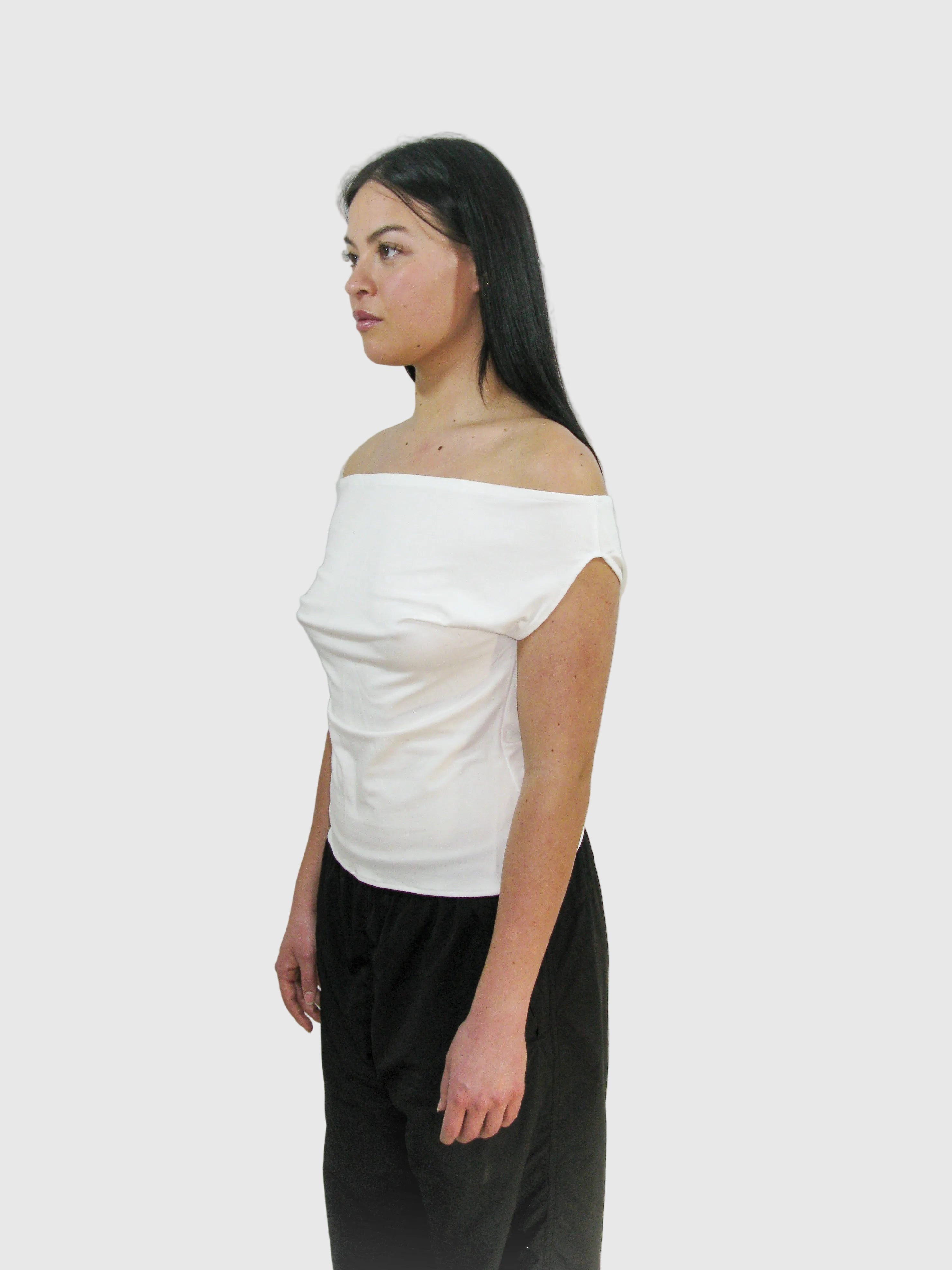Woman wearing a white off-shoulder top and black pants against a plain background